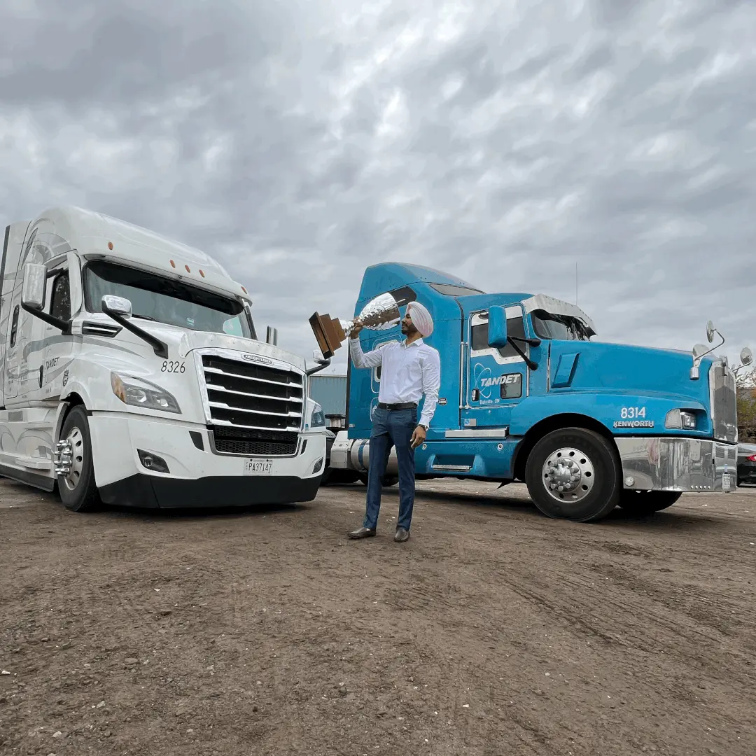 TANDET driver holding a large trophy between a white and a blue truck.