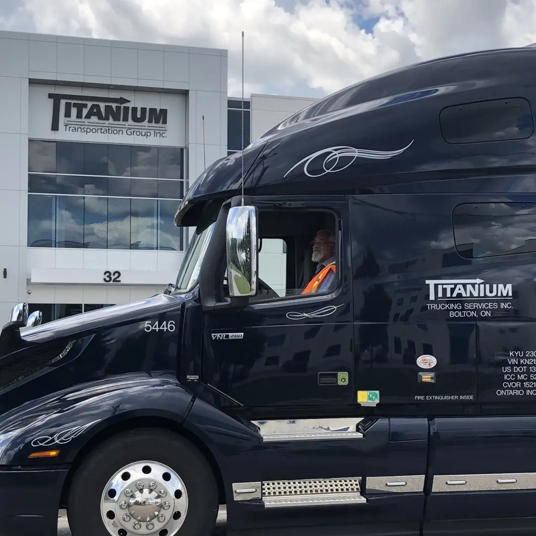 Titanium Transportation Group driver in a dark blue Volvo VNL outside company headquarters.
