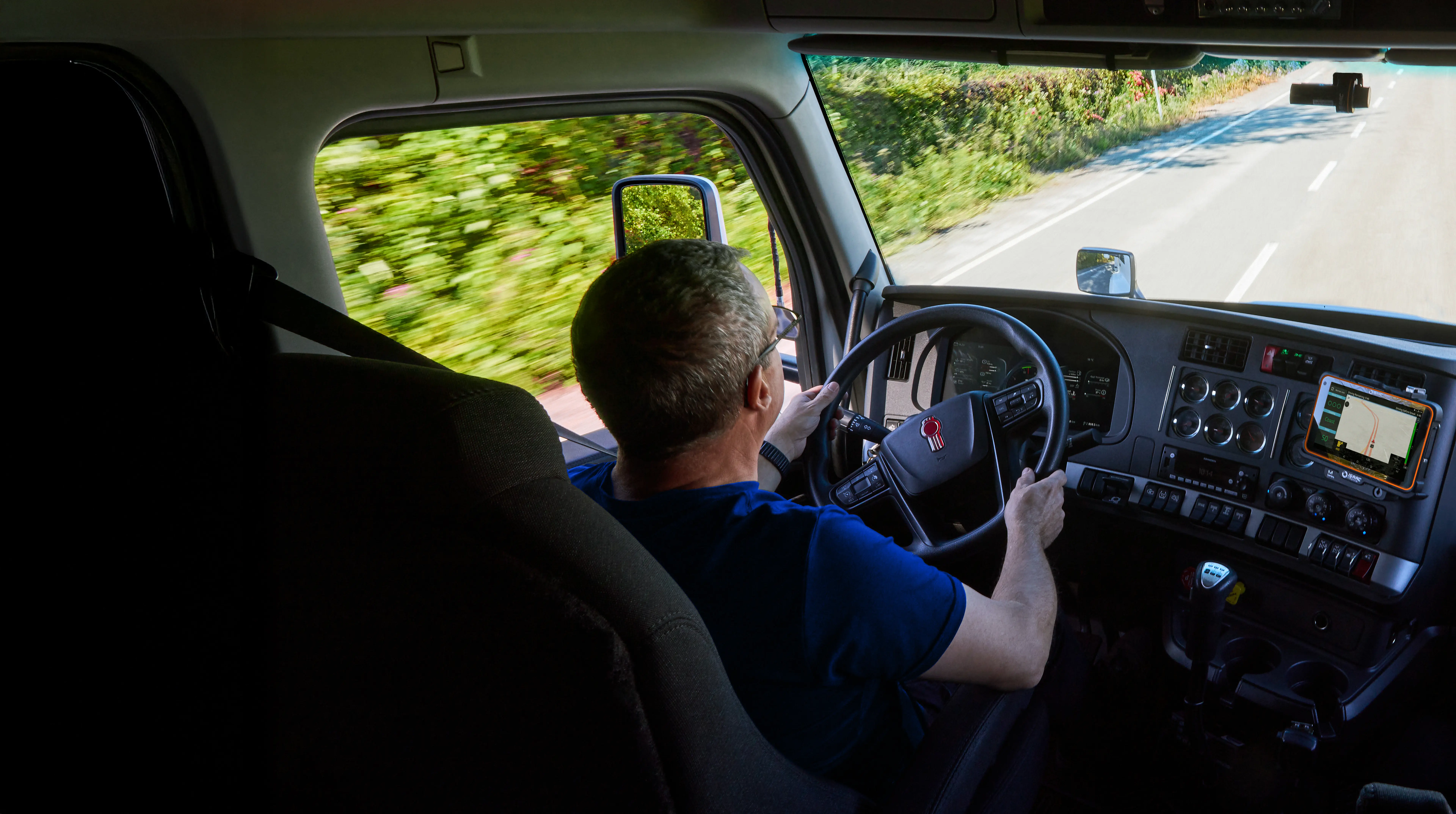 Mill Creek Truck Driver in Cab Mill Creek truck driver steering inside the cab with dashboard controls and a navigation/ELD tablet.