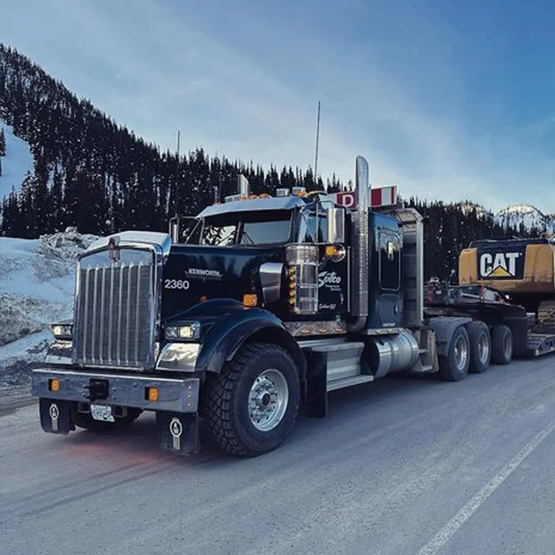 Sutco Kenworth heavy-haul truck towing equipment on a snowy mountain road.
