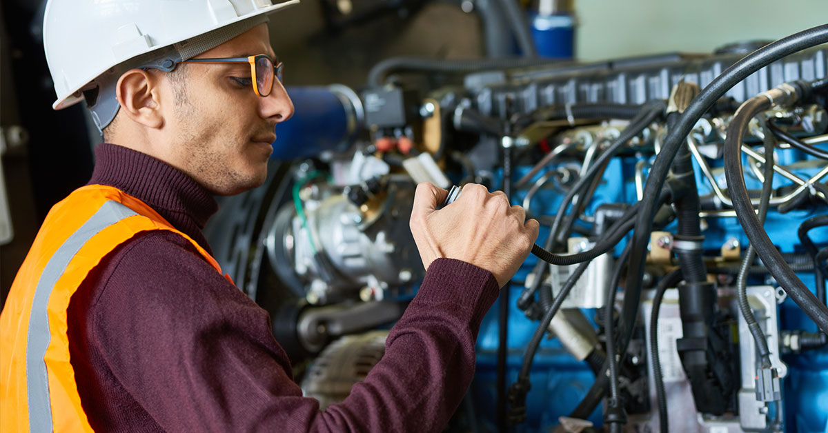 A worker in a hard hat and vest working on repairing an asset of heavy machinery for a business.