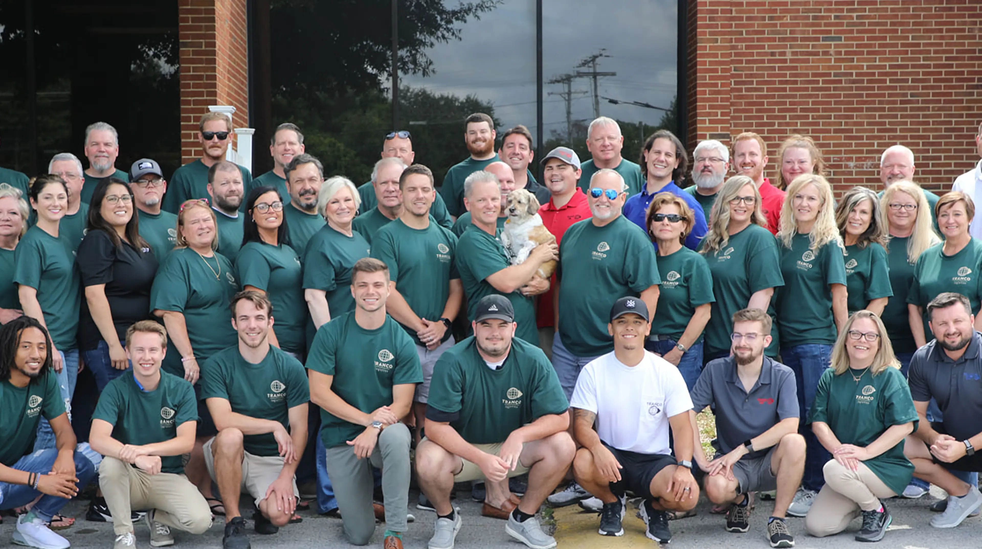 Group photo of the Tranco Logistics team gathered outside the office, many wearing green shirts.
