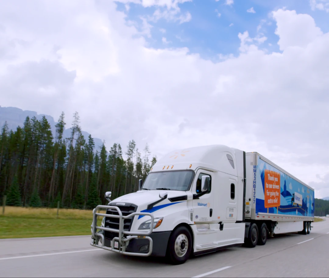 Walmart semi-truck en route through a scenic mountainous region under a partly cloudy sky.