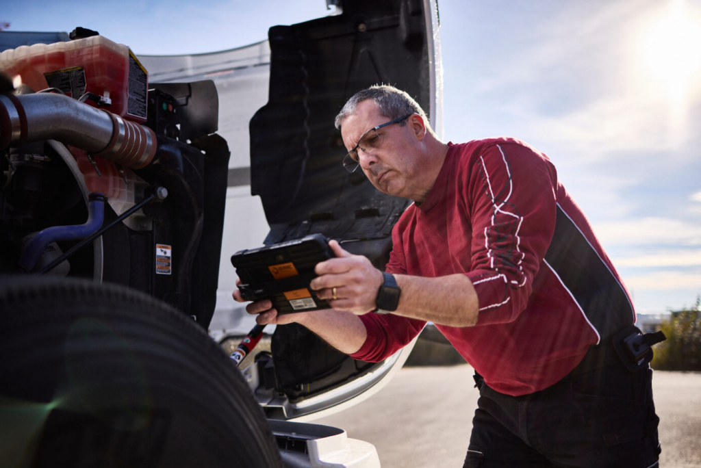 Technician using ISAAC's rugged tablet for real-time diagnostics on a tank truck's engine, ensuring peak performance and safety.