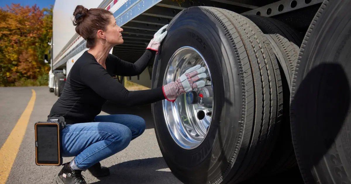 A vigilant fleet professional conducts a detailed pre-departure tire inspection on a commercial truck, employing ISAAC Instruments technology to ensure safety and compliance.