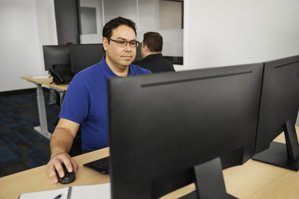 Office worker monitoring cybersecurity systems on dual monitors.