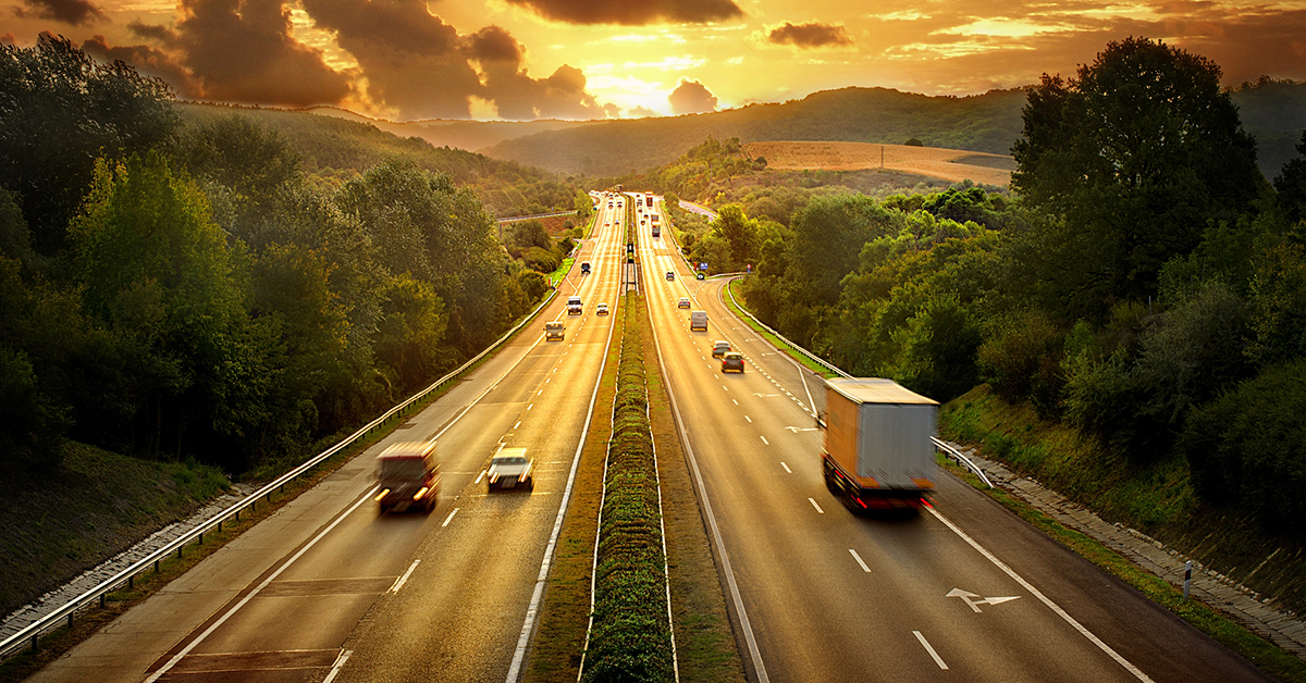 Trucks driving on a freeway at sunset.