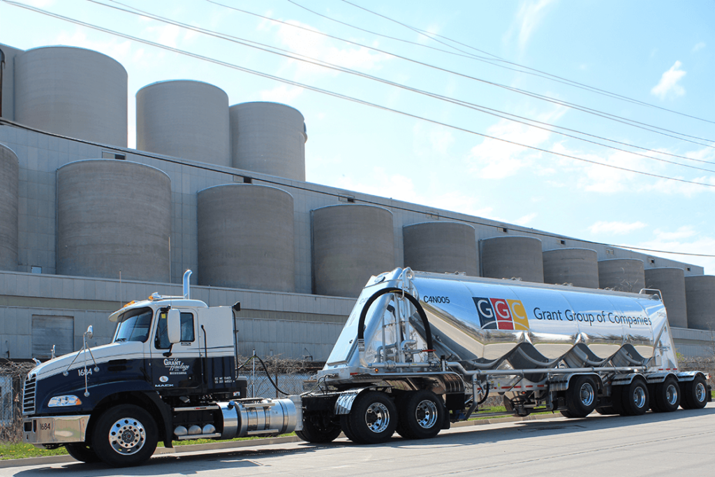 Grant Group of Companies semi-truck parked in front of large industrial silos under a blue sky.