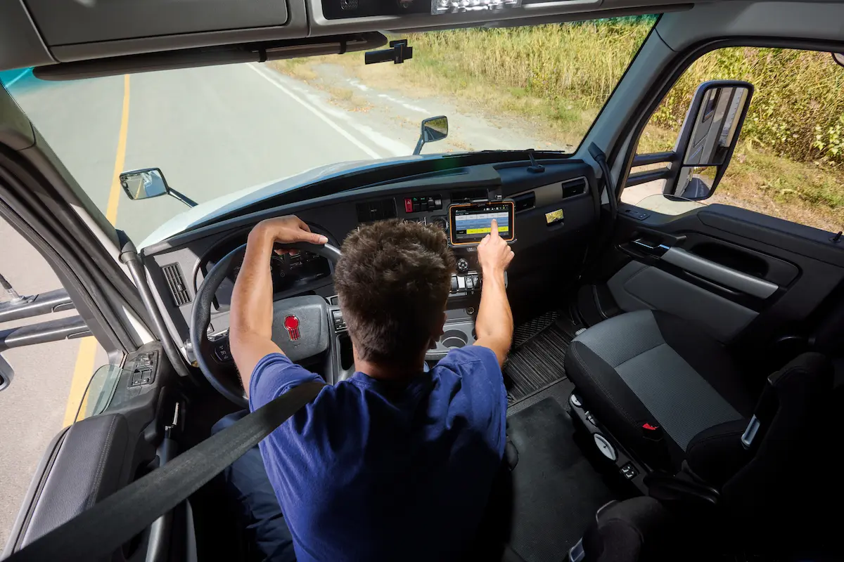 Truck driver interacts with ISAAC ELD tablet while driving, ensuring compliance with the 16-hour short-haul exemption rule
