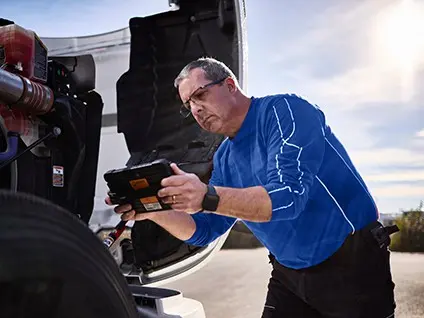 Technician inspecting a truck engine using a rugged tablet for preventive maintenance data