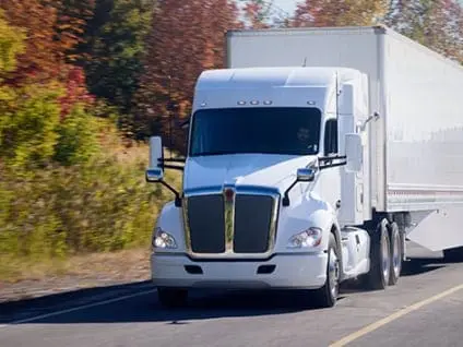White semi-truck driving on a rural road in autumn, symbolizing reduced CO2 emissions