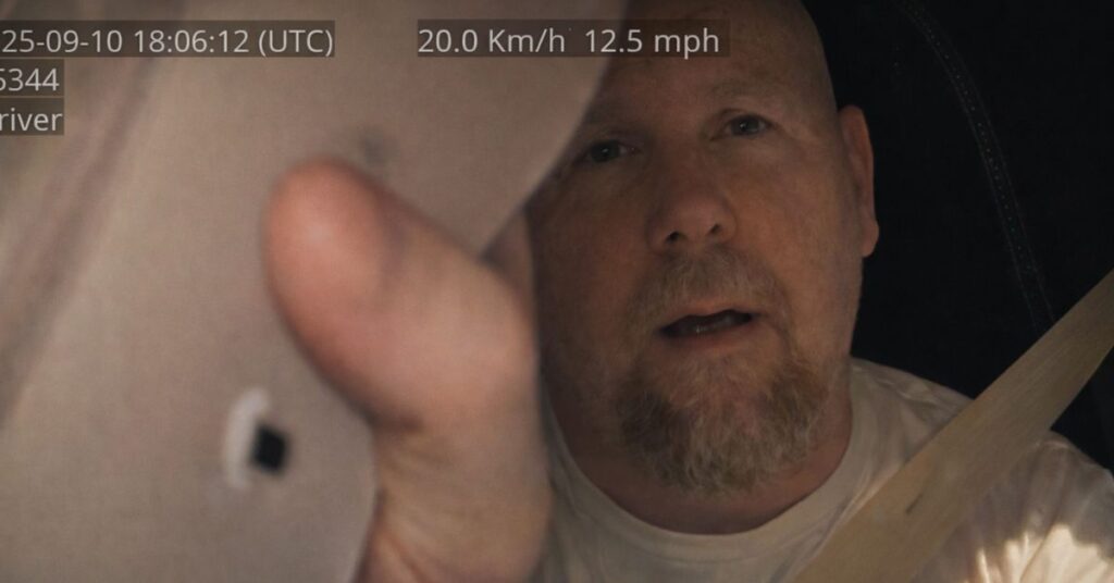 In-cab camera view of a driver reaching up to cover the lens with his cap